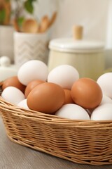 Raw chicken eggs in wicker basket on wooden counter indoors, closeup
