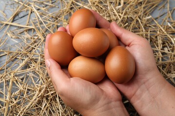 Woman with raw chicken eggs and straw at grey wooden table, closeup