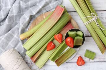 Rhubarb stalks and strawberries on white wooden table, flat lay