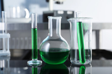 Different glassware with green liquid on table in laboratory, closeup