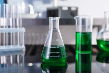 Glass flask and other glassware with green liquid on table in laboratory, closeup