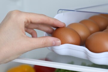 Woman taking raw chicken egg from container in fridge, closeup