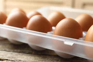 Raw chicken eggs in container on wooden table, closeup