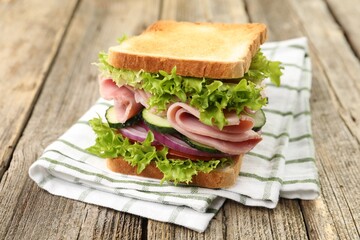 Tasty sandwich with ham and vegetables on wooden table, closeup
