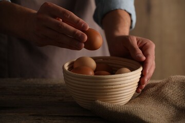 Man putting raw chicken egg into bowl at wooden table, closeup
