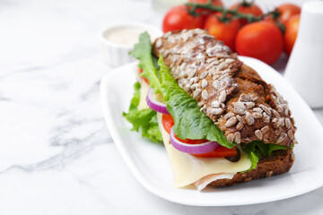 Tasty ciabatta sandwich with cheese and vegetables on white marble table, closeup. Space for text