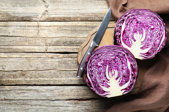 Halves of fresh red cabbage and knife on wooden table, flat lay. Space for text