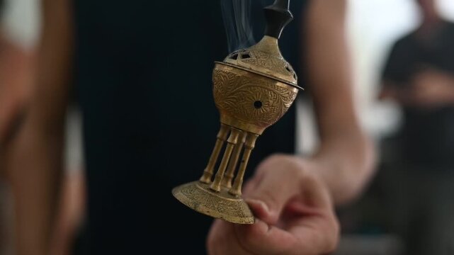 Person holding a traditional brass incense burner with smoke