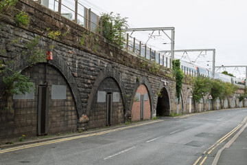 Fototapeta premium Railway viaduct storage arches sealed with doors and metal panels beneath active train tracks, highlighting urban decay, history, and industrial architecture.