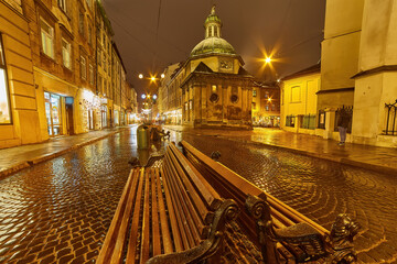 Historic European city square with a wet cobblestone street at night.