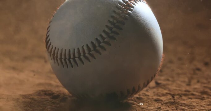 Close-up cinematic shot of a baseball on dusty ground, wind blowing dust and dirt around the ball. Soft dramatic lighting adds atmosphere and motion.