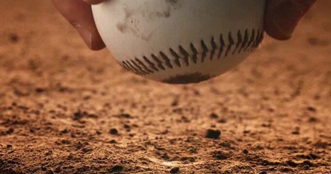 Close-up cinematic shot of a baseball on dusty ground being picked up by a player&rsquo;s hand. Dust rises in soft dramatic lighting, emphasizing detail and motion.
