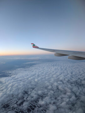 Wing of Middle East Airlines plane flying above a thick cloud layer with clear blue sky and soft pastel tones during a peaceful high-altitude flight over land