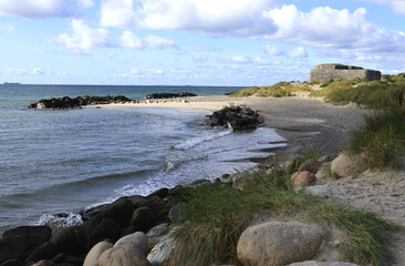 Landscape photo with a view of a bay of sea, a sandy beach with large stones in the foreground and a bunker on the coast at Cape Grenen, in Skagen, northern Denmark