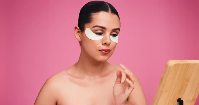Eye patches, mirror and woman in studio, beauty and dermatology on pink background. Mockup space, reflection and person with healthy skin, aesthetic and wellness with shine, confidence and glow