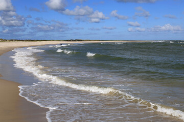 Landscape photo with a view of a bay of sea and sandy beach against a blue sky with clouds at Cape Grenen, in Skagen, northern Denmark