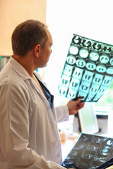 Doctor holding and examining MRI or CT scan images with human organs in light. Concept of medical diagnostics, radiology, examination and health research.