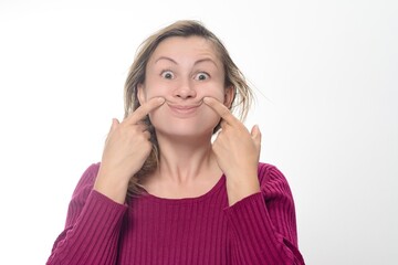 Woman forcing a smile. A woman with a maroon sweater on a white background uses her fingers to force the corners of her mouth into a smile.
