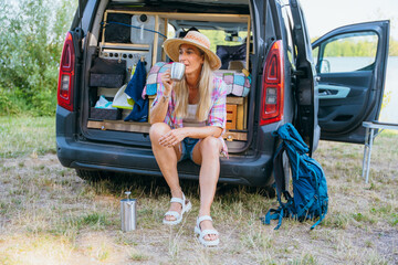 Woman rests at her minivan with coffee after a lake hike enjoying solitude, freedom, and camping in nature
