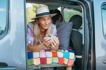 Woman embraces the freedom of vanlife as she drinks coffee alone in her mini campervan by a quiet nature spot