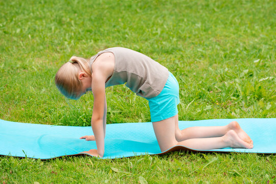 Blonde Generation Alpha girl doing cat pose yoga on a mat outdoors in the summer in the courtyard of a country house.