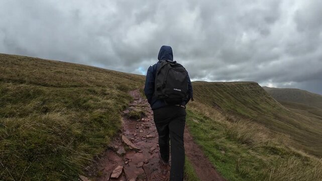 Scenic view of a man walking towards the Pen y Fan summit in Brecon Beacons National Park. Captures lush grassland, dramatic sky, and mountainous backdrop, conveying adventure and tranquility.