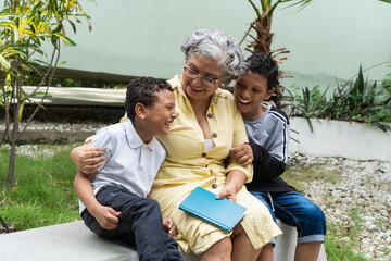 Grandmother laughing with grandchildren reading book outdoors