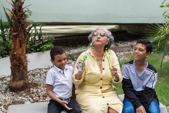Grandmother playing with grandchildren blowing soap bubbles outdoors