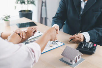 Close up of real estate agent and client shaking hands with house model, contract paperwork and...