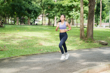Young Asian woman running on a paved path in a lush green park, concentrating on her fitness routine and enjoying an active outdoor workout in sportswear
