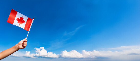青空を背景に子供の手が小さなカナダの国旗を持っている。(Child's hand holding a small Canada flag on blue sky.)
