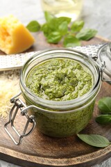 Fresh pesto sauce in jar, grater and ingredients on grey table, closeup