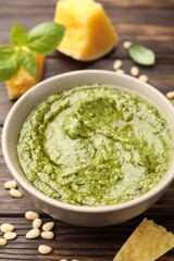 Fresh pesto sauce in bowl and ingredients on wooden table, closeup