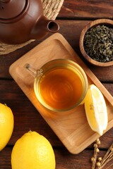 Aromatic tea in cup with lemons, dry leaves and teapot on wooden table, flat lay
