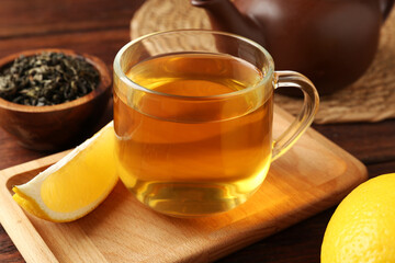 Aromatic tea in cup with lemons and dry leaves on wooden table, closeup