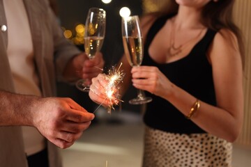 Friends celebrating New Year with sparklers and wine glasses indoors, closeup