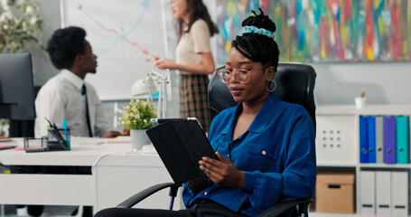 In a professional setting, employees work on a project, analyzing data on the blackboard, while a woman in a blue shirt, ignoring the task, plays games on her tablet.