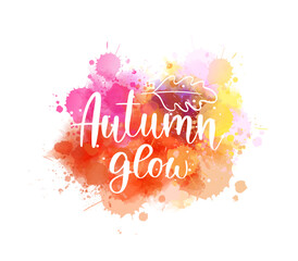 Colorful handwritten text 'Autumn glow' on watercolor orange paint splashes. Seasonal modern calligraphy lettering text