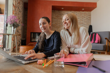 Two students sitting on the living room floor with a laptop, folders and notebooks, smiling while working together. Concept of learning, teamwork and friendship. Indoor horizontal with balcony view.
