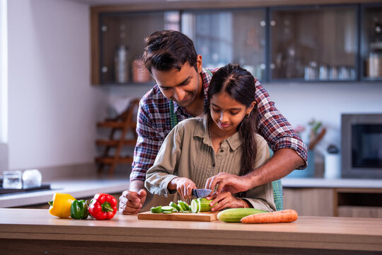 Indian father and daughter chopping cucumber, sharing joyful bonding at home