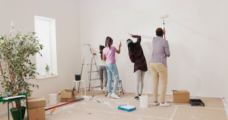 Crazy close-knit family paints walls with white paint using rollers, they dance in the middle of the room, sing, parents play with children, the house prepared for renovation