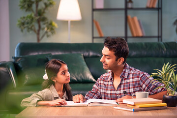 Indian Father helping daughter study from textbook, family learning moment at home