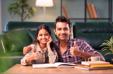 Fototapeta premium Indian Father helping daughter study from textbook, family learning moment at home