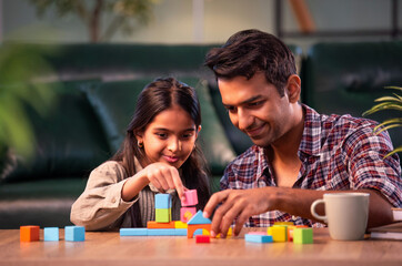 Fototapeta premium Indian father and daughter building wooden toy tower, spending quality time together