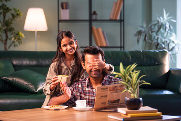 Fototapeta premium Indian Daughter surprising father with gift, hugging and sharing loving family moment at home