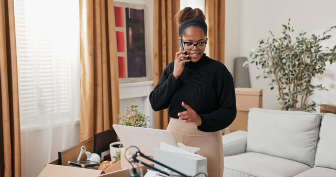 In her new apartment, a woman uses a laptop to browse furniture stores online. She holds her phone to her ear, calling a hotline to get details about products and delivery options. - Powered by Adobe