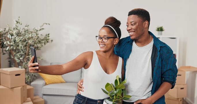 A woman holds a plant in a pot and smiles while taking a selfie with her boyfriend. The couple just moved into their new apartment and shares the moment on social media. - Powered by Adobe