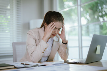 Frustrated businesswoman sitting at desk looking at laptop, feeling stressed and confused while working in modern office.