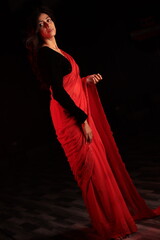 Fototapeta premium Portrait of an Indian Nepali woman in red traditional saree and black blouse under warm indoor lighting
