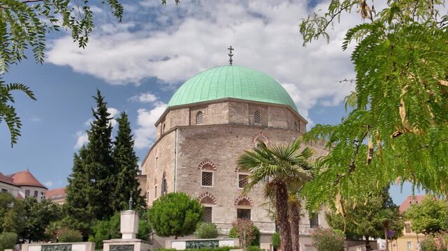 Exterior view of the Mosque of Pasha Qasim in P&eacute;cs, beautifully framed by a tree, highlighting its ornate architecture and historic charm